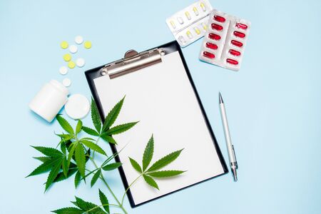 Top view of blank paper for writing doctor prescription. Marijuana leaf with medical pills on blue...