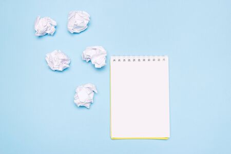 Open empty notebook and crumpled paper balls on blue paper background. Creation process, idea or...