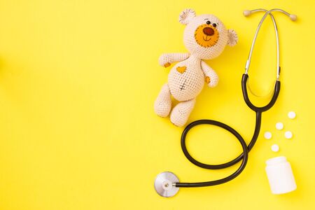 Children's toy teddy bear amigurumi with stethoscope on yellow background with copy space. Child health concept. Top view, flat lay.の写真素材