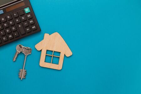 Closeup of house wooden model and keys with calculator on blue background. Mortgage property insurance buy dream home shopping sale rent concept. Top view, flat lay.の写真素材