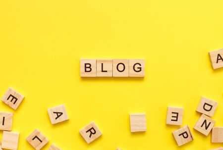 Wooden cubes letters with the word blog on a yellow background. Top view, flat lay, copy space