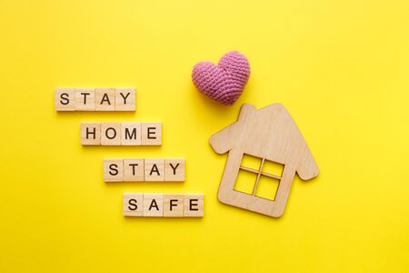 Stay Home text with wooden house with knitted heart on yellow background. Quarantine concept, covid-19 virus protection. Top view, flat layの写真素材