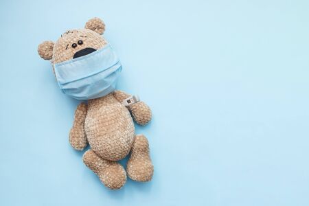 Cute teddy bear with face mask on his mouth on blue background. Quarantine concept, covid-19 virus protection. Flat lay, top view, copy spaceの写真素材