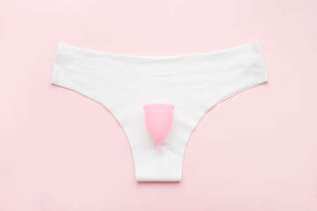 White pantie with menstrual cup on pastel pink colorful background. Flat lay, pantie, menstrual cup. Menstruation, feminine hygiene, woman's health, zero waste conceptの写真素材