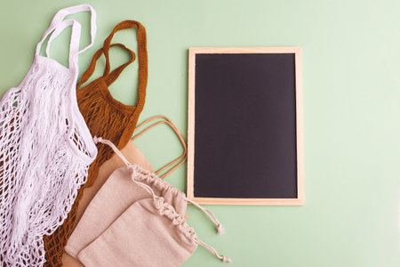 Canvas bags with drawstring, mockup of small eco sack made from natural cotton fabric cloth with blackboard flat lay on green pastel background from top view.の写真素材