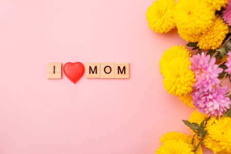 Wooden letters in the phrase I love mom with flowers on a pink background. Greeting card concept for mother day.の写真素材
