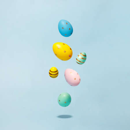 Colored easter decorated eggs flying on a blue background. Easter greeting card in minimalist style...