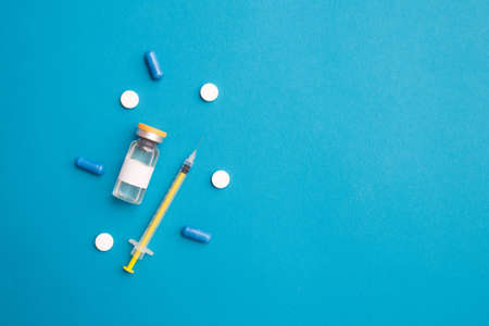 Inscription coronavirus vaccine in glass bottle syringe and pills on blue background with copy space . Concept of vaccination against Covid 19. Top view, flat layの写真素材