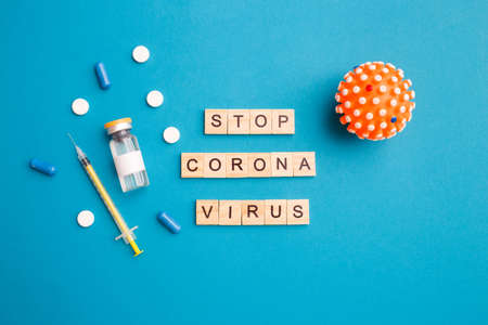 Wooden letters in phrase stop coronavirus. Vaccine in glass bottle syringe and pills on blue background with copy space . Concept of vaccination against Covid 19. Top view, flat layの写真素材