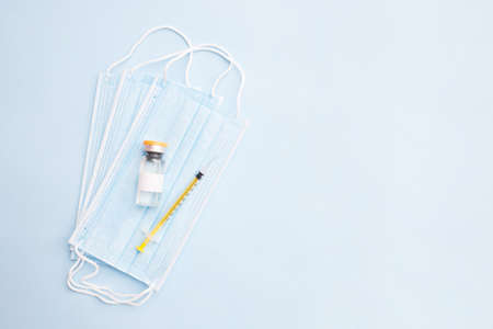 Inscription virus vaccine in glass bottle syringe and medical mask on blue background with copy spaceの写真素材