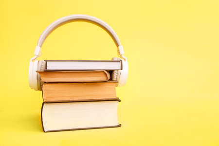 Books with white modern headphones on yellow background. Listen to the audio book conceptの写真素材