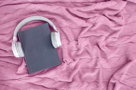 Book with white modern headphones flat lay on pink knitted blanket. Listen to the audio book conceptの写真素材