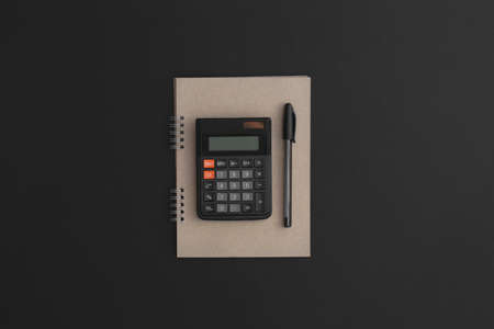 Calculator, notebook, pen on black leather background.