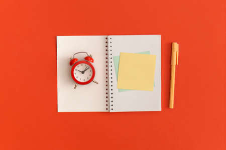 Red alarm clock and notebooks with space for text on red backgroundの写真素材