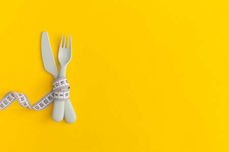 Measuring tape and cutlery on yellow background. Weight loss conceptの写真素材