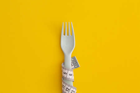 Measuring tape and cutlery on yellow background. Weight loss conceptの写真素材