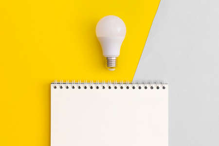 Notebook and light bulb on yellow background. top view. flat lay.