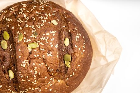 Tasty fresh baked loaf of dark bread with sesame seeds on hite background with paper cower