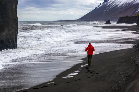 man in red jacket taking photo of waves on the Atlantic ocean in Iceland