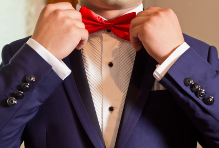 Groom in a white shirt and blue suit correcting red bow tieの写真素材