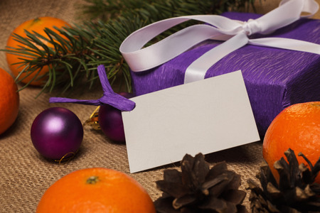Purple gift with postcard, orange tangerines, fir-cones, Christmas decorations and fur-tree branchの写真素材