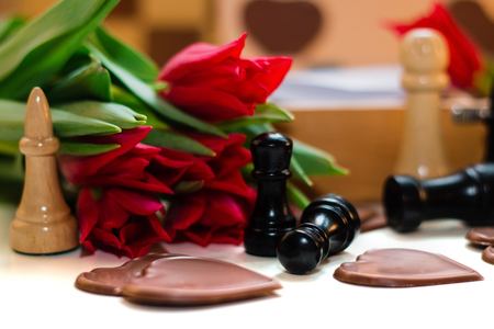 Bouquet of red tulips, chocolates in a shape of a heart and chessの写真素材