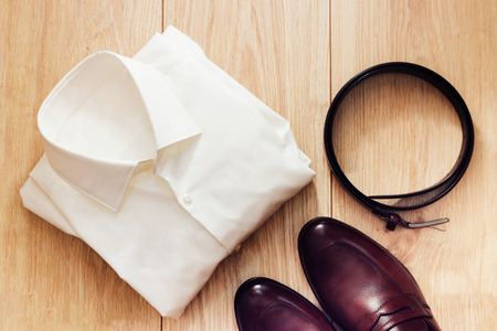 Flat lay set of classic men`s clothes such as brown shoes, belt and white shirt on wooden background. Top view.の写真素材