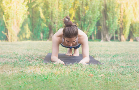Slim woman practicing sport in nature -  plank pose. Female balancing on mat on green background....