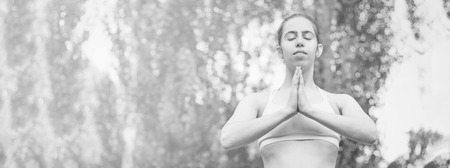 Slim young woman practicing yoga in nature, meditating in a yoga pose, holding arms together. Green background. Good healthy and sport concept. Front view. Copy space for text. Black and white photo.の写真素材
