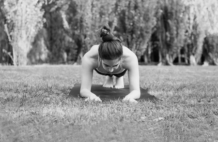 Slim woman practicing sport in nature -  plank pose. Female balancing on mat. Healthy and sport concept. Black and white photo. Front view.の写真素材