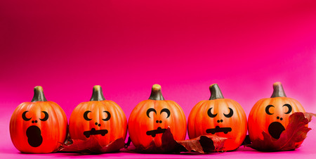 Halloween holiday background. Halloween pumpkin jack o lantern decor with funny faces on pink...