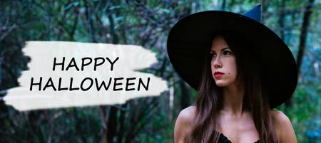 Halloween holiday background. Halloween Witch in a dark forest. Beautiful young woman in witches hat and costume with text happy halloween.の写真素材