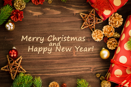 Christmas and New Year's Day festive decoration, red and golden balls, fir cones and wooden stars with present wrapped in red paper with golden circles on brown wood background with text Merry Christmas and Happy New Year. Flat lay. View from above.の写真素材