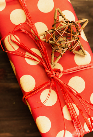 Christmas and New Year's Day festive decoration, wooden star with present wrapped in red paper with golden circles on brown wood background. Flat lay. View from above. Copy space for text.の写真素材