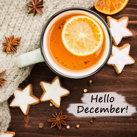 Winter theme. Hot tea with spices, orange, anise, cookies in a shape of star, pepper and gray scarf on wooden background. Flat lay, View from above with text hello December.の写真素材