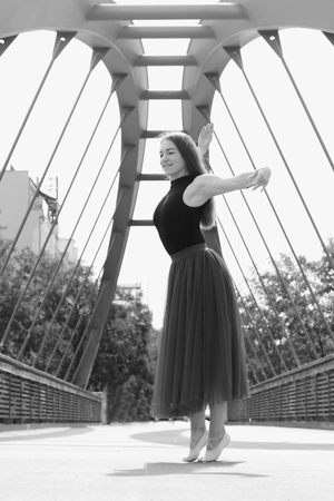 Young slim beautiful woman with long brown hair dancing and smiling outdoors in black shirt and terracotta (red pear) long skirt. Sport and healthy conÑept. Black and white photo.の写真素材