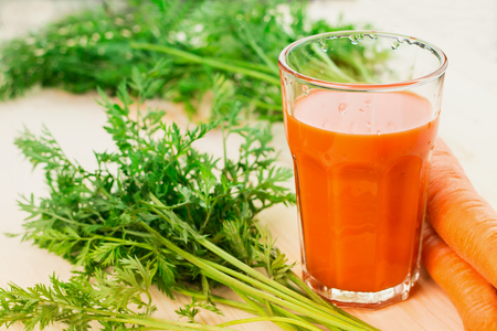 Fresh carrot juice in glass with carrots and green carrot tops on wooden table background. Healthy lifestyle concept.の写真素材