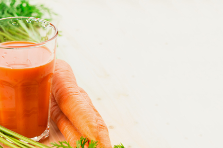 Fresh carrot juice in glass with carrots and green carrot tops on wooden table background. Healthy lifestyle concept. Copy space for text.の写真素材