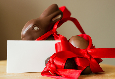 Big and small chocolate Easter eggs, traditional Easter chocolate Bunny decorated with red ribbon on pastel background. Holiday Easter background with copy space for text.の写真素材