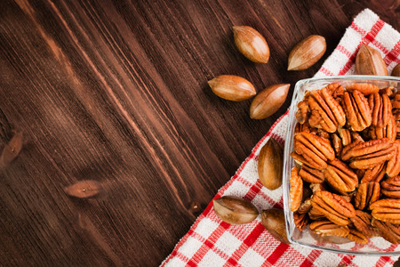 Pecan nuts in the shell with pecan kernel in glass bowl on wooden background. Red checkered tablecloth. The concept of proper nutrition, vitamins and minerals, antioxidants. Copy space for text. Top view.の写真素材