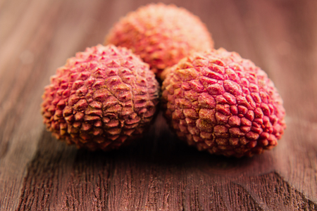 Three fresh organic lychee fruits on brown wooden background. Tropical fruit. Macro view.の写真素材