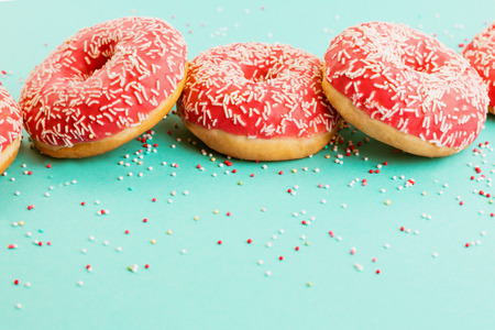 Three coral donuts lying in a line. Donuts decorated with icing on blue background. Top view. Copy space for text.の写真素材