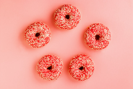 Five coral donuts lying in a round. Donuts decorated with icing on pink background. Top view.の写真素材