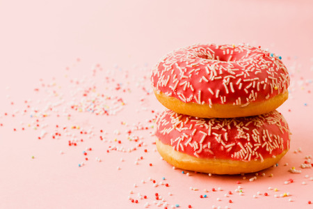 Two coral donuts standing in a line. Donuts decorated with icing on pink background. Copy space for text.の写真素材