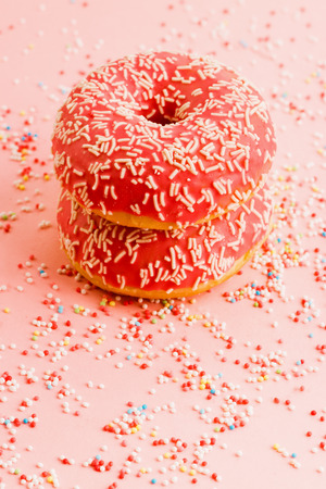 Two coral donuts standing in a line. Donuts decorated with icing on pink background. Copy space for text.の写真素材