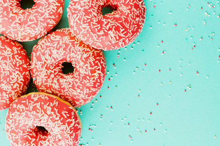 Five coral donuts lying in a corner. Donuts decorated with icing on blue background. Top view. Copy space for text.の写真素材