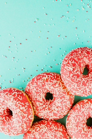 Five coral donuts lying in a corner. Donuts decorated with icing on blue background. Top view. Copy space for text.の写真素材