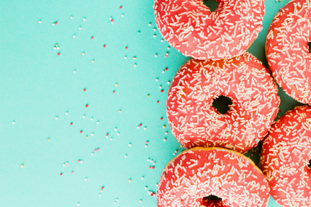Five coral donuts lying in a line. Donuts decorated with icing on blue background. Top view. Copy space for text.の写真素材