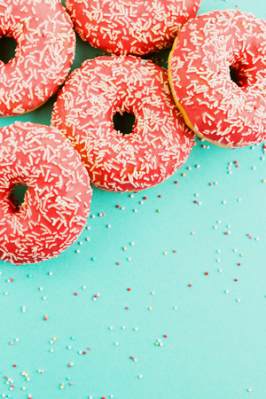 Five coral donuts lying in a corner. Donuts decorated with icing on blue background. Top view. Copy space for text.の写真素材