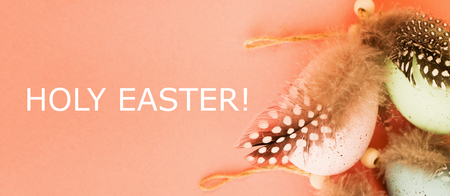 Green pastel big Easter eggs decorated with ribbon and bird feather on coral background. Holiday Easter background with text Holy Easter. Top view.の写真素材